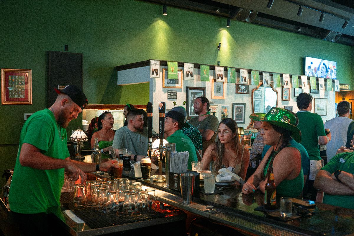 Bartender serving guests in green leprechaun hats at the bar on St. Patrick's Day